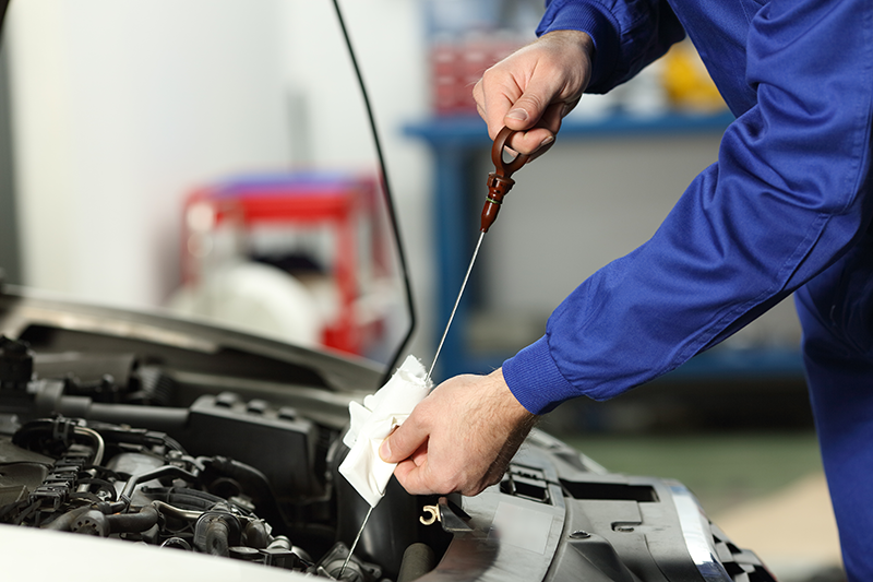 A mechanic checking an oil dipstick - Why Oil Changes Still Matter on a Packed Workday